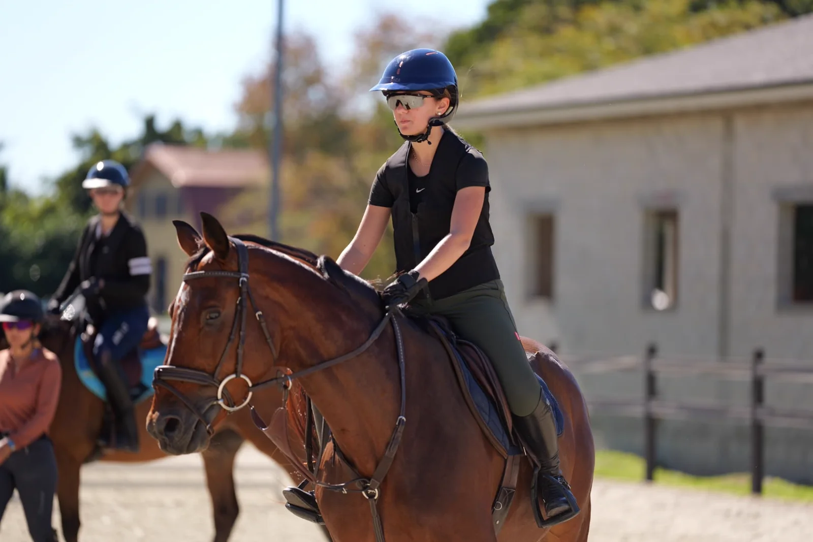 Rider schooling a bay horse in the ring at L'Écurie Equestrian Club, with other riders in the background