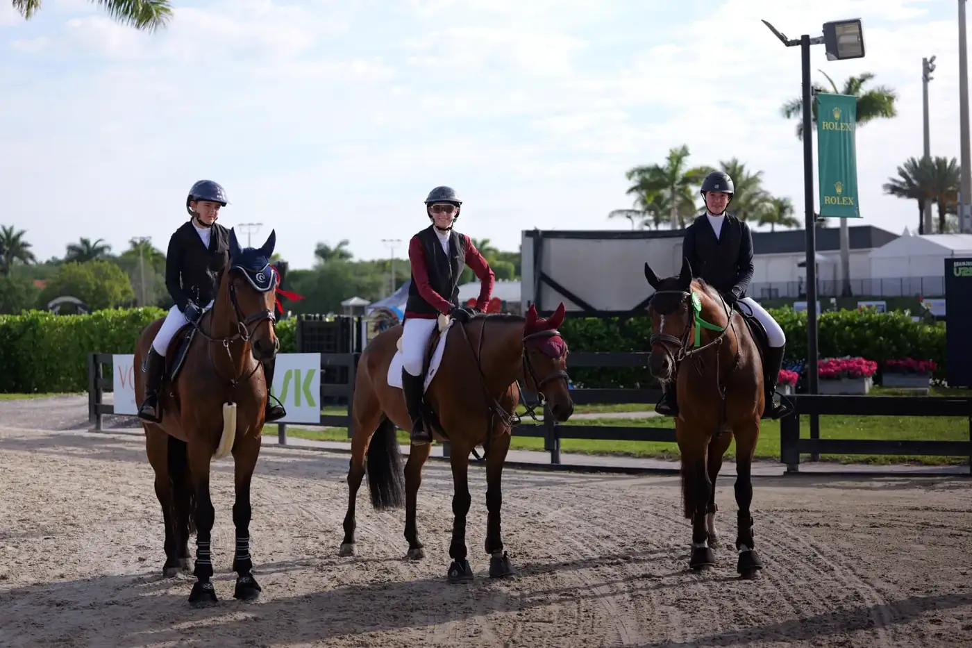 Three L'Écurie riders on bay horses in the sand arena at a Florida show venue